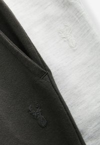 Două bucăți de țesătură: una verde închis și una gri deschis, fiecare cu un logo subtil embosat. Textură moale cu cusături plate.