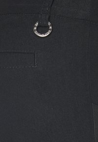 Μαύρο παντελόνι από υφ�αντό ύφασμα, με μια μικρή κυκλική μεταλλική λεπτομέρεια και μια πλευρική τσέπη με αντίθετη ραφή.