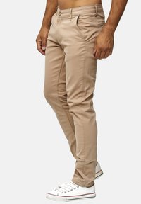 Jasno beżowe chinosy o slim fit, z przednimi kieszeniami i jedną tylną kieszenią, połączone z białymi sneakersami.