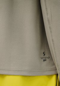 Beżowa tkanina o fakturze z małymi perforacjami i czarnym logo „sorona AGILE”, nałożona warstwowo na jasnofioletową gładką tkaninę.