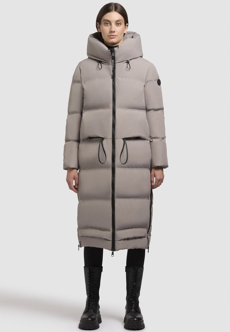 Ljust grå, vadderad lång kappa med huva, frontdragkedja, dragsko i midjan och svarta detaljer; har en strömlinjeformad silhuett och långa ärmar.