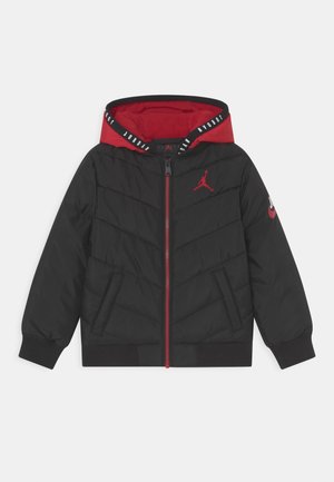 Chaqueta acolchada negra con capucha interior roja, cremallera frontal, logo Jumpman rojo en el pecho y el símbolo Nike en la manga izquierda.