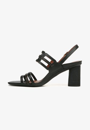 Black leather heeled sandal with wide straps, square toe, and ankle strap featuring a cutout design. Chunky black heel, smooth texture.