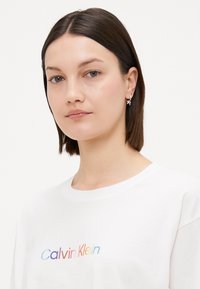 Hvit bomulls T-skjorte med avslappet passform, med en flerfarget "Calvin Klein" logo. Korte ermer og rund hals, med jevn tekstur.