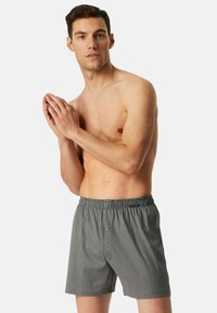 Boxers rayés gris en tissu léger avec une taille élastique et un détail de bouton unique à l'avant.