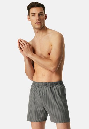 Boxers rayés gris en tissu léger avec une taille élastique et un détail de bouton unique à l'avant.
