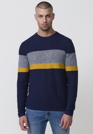 Suéter azul marino con textura acanalada; presenta rayas horizontales grises y mostaza en el pecho. Cuello redondo y mangas largas.