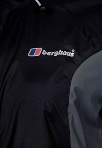 Černá a šedá bunda s logem "berghaus" v bílé a červené barvě. Materiál vypadá hladce, s jemným leskem a kontrastními texturovanými panely.