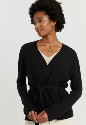 Cardigan nero avvolgente in tessuto morbido, con vita annodata e maniche lunghe, polsini a coste e scollatura profonda a V.