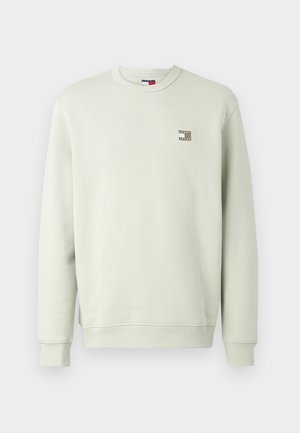 Sweatshirt vert clair avec un col rond et des poignets côtelés. Présente un petit patch logo marron sur la poitrine gauche. Texture de tissu douce.