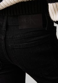 Schwarze Denim-Jeans mit glatter Textur, Standardtaschen und einem Calvin Klein-Label am Bund, das ein minimalistisches Design präsentiert.