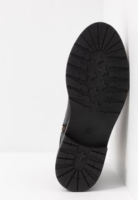 Bota de cuero negra con suela de goma robusta. Tiene una superficie texturizada y una cremallera lateral para facilitar su uso. Patrón de agarre resistente en la suela.
