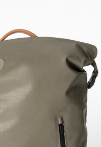 Borsa pieghevole in tessuto verde oliva con manico in pelle, dotata di una tasca con zip e di una tracolla regolabile con fibbia.