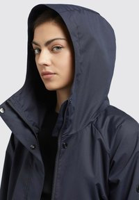 Navy waterproof jacket with a hood, featuring zip closure and snap buttons, smooth texture, and a fitted design.