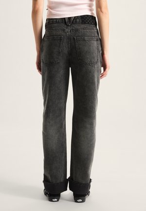 Black denim jeans with a faded grey finish, straight-leg fit, frayed hem, and two back pockets. The waistband features a checkerboard pattern.