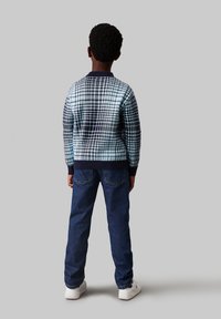 Maglione lavorato a maglia in un motivo a quadri blu chiaro e blu navy, con colletto e polsini a coste, abbinato a jeans blu scuro e sneakers bianche.