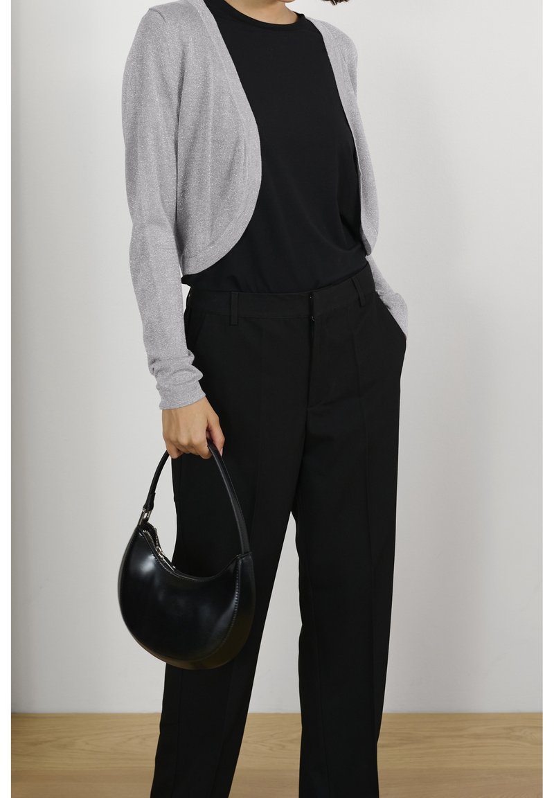 Cardigan gris clair au design épuré, porté sur un haut noir, associé à un pantalon plissé noir et un sac à main noir incurvé.