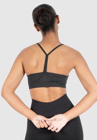 Musta urheiluliivit, joissa on kilpailijantakaosa ja teksturoidut paneelit. Materiaali näyttää joustavalta ja vartalonmyötäiseltä, yhdistettynä korkeavyötäröisiin mustiin leggings-housuihin.