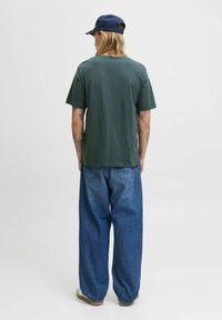 Kortærmet, mørkegrøn bomulds t-shirt parret med løstsiddende, lys blå denim jeans. Komplementeret af en navy cap og lyse sko.