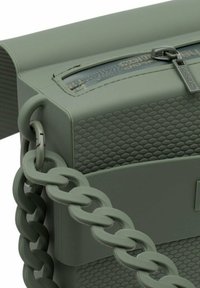 Borsa verde in gomma con superficie testurizzata, apertura con zip e grande manico a catena. Il design è squadrato con bordi morbidi.
