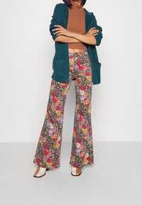 Uppblåsta blommiga byxor med en brun bakgrund som har röda, gula och lila blommor; kombinerat med en teal-färgad kofta och en brun topp.