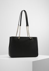 Sac cabas noir en matériau texturé, doté de doubles anses d'épaule, d'accents en chaîne, et d'une forme rectangulaire structurée.