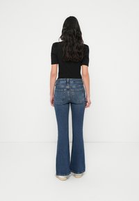 Εφαρμοστό μαύρο τοπ συνδυασμένο με καμπανέ μπλε τζιν. Το τζιν διαθέτει ψηλή μέση, δύο πίσω τσέπες και ανοιχτό πλύσιμο με διακριτική ξεθώριαση.