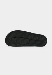 Semelle de chaussure noire avec motifs de sculptures circulaires et linéaires pour l'adhérence, présentée à plat sur un fond clair.