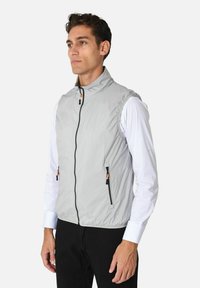 Gilet grigio leggero con colletto alto, zip frontale e due tasche con zip. Presenta una texture del tessuto e zip arancioni.