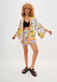Floral kimono in pastel colors, featuring wide sleeves and an open front. Paired with a black crop top and a matching printed skirt. Black sandals.