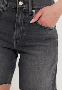 Pantalones cortos de mezclilla gris oscuro con dobladillo deshilachado, que presentan un bolsillo frontal, cierre de botón y detalles de costura visibles.