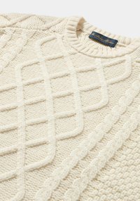 Kremowy sweter z dzianiny warkoczowej, z teksturowanym wzorem ukośnym i krzyżowym. Z prążkowanym dekoltem i miękką teksturą tkaniny.