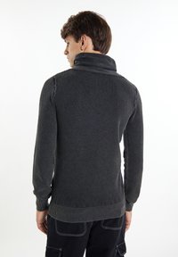 Dunkelgrauer Pullover mit hohem Kragen, strukturiertem Strickmuster und gerippten Bündchen und Saum. Das Material wirkt weich und bequem.