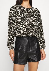 Schwarz-ivory Leopardenmuster-Bluse mit langen Ärmeln, rundem Ausschnitt und lockerer Passform, kombiniert mit hochgeschnittenen schwarzen Ledershorts.