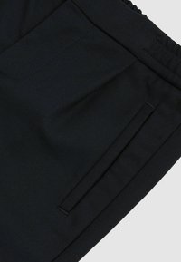 Mustad musta kangast lühikesed püksid, millel on sile tekstuur, elastne vöökoht ja küljetasku, millel on peenelt tikandiga kaunistus.