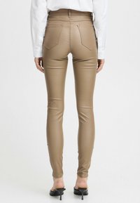 Pantalons skinny en simili cuir beige avec poches arrière, design ajusté, taille mi-haute, et accompagnés de mules à talons noirs.
