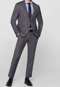 Completo grigio su misura con revers a punta, pantaloni davanti piatti, camicia azzurra e cravatta blu navy a pois, abbinato a scarpe in pelle nere.
