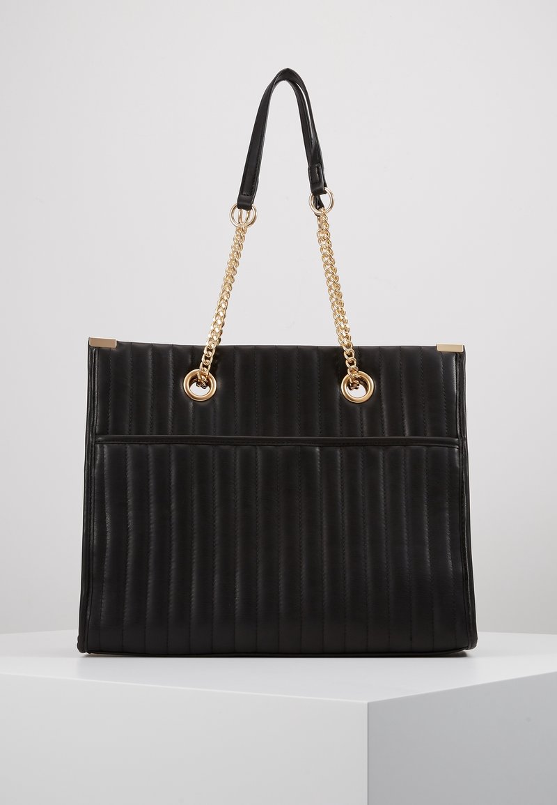 Sac à main rectangulaire noir avec matelassage vertical, anses en chaîne dorée fixées par des œillets ronds dorés, et petits accents dorés aux coins.