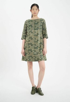 Robe verte à motifs avec des manches trois-quarts, présentant un design géométrique et une coupe ample. Le mannequin porte des chaussures à enfiler vert olive.