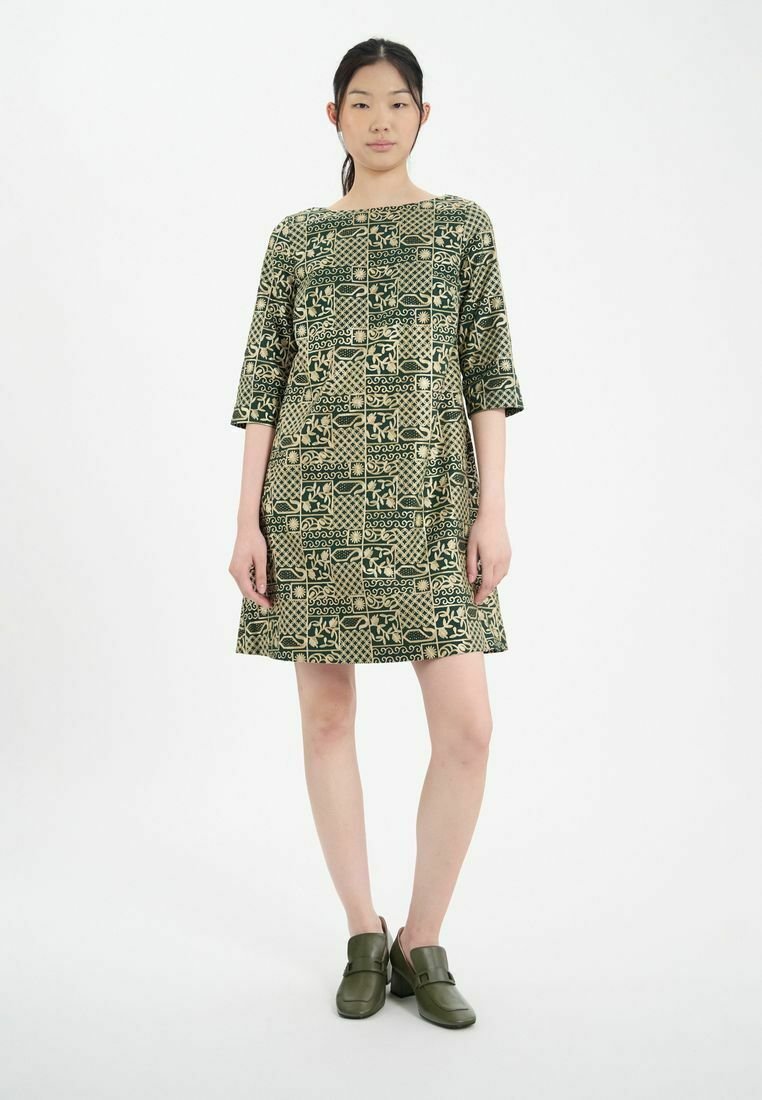 Robe verte à motifs avec des manches trois-quarts, présentant un design géométrique et une coupe ample. Le mannequin porte des chaussures à enfiler vert olive.