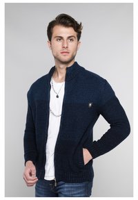 Marineblaue Strickjacke mit hohem Kragen, Reißverschluss und Fronttaschen. Verfügt über einen strukturierten Stoff und ein dezentes Logo-Detail auf der Brust.