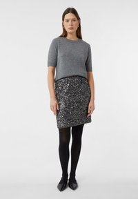 Szary sweter z krótkim rękawem w połączeniu z błyszczącą czarną spódnicą z cekinów. Stylizację dopełniają czarne rajstopy i czarne baleriny na szpic. Prosty, nowoczesny design.