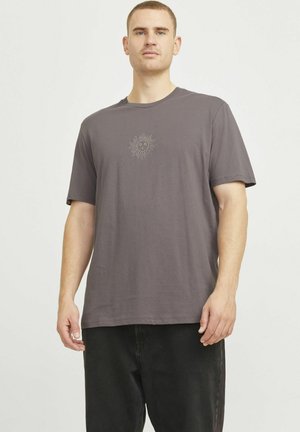 Graues Baumwoll-T-Shirt mit lockerer Passform, mit einem Sonnenmotiv in der Mitte. Kurze Ärmel und Rundhalsausschnitt. Getragen mit schwarzen Hosen.