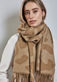 Sciarpa tan con motivo leopardato, realizzata in tessuto morbido. Presenta bordi frangiati e un design avvolgente per garantire calore.