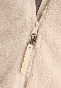 Kermarus väri fleece-kangas, jossa on pörröinen rakenne. Zipperin vedin on varustettu "Cecil"-brändillä ja metalliklipsillä.