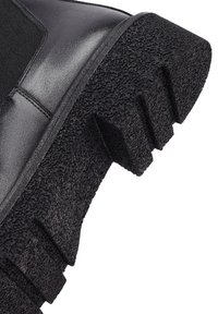 Czarna skórzana botka z teksturowaną gumową podeszwą, wyposażona w grubą bieżnię i elastyczne boki dla pewnego dopasowania. Gładka cholewka i wzmocniony dziób.