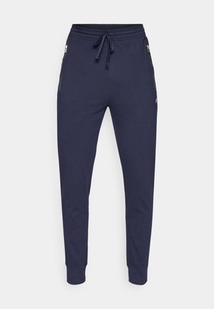 Tamsiai mėlyni sportiniai džinsai su elastinga juostele, raišteliu ir priekinėmis užtrauktukų kišenėmis. Lygus audinys su elastingais sutrauktais vamzdžiais ties kulkšnimis.