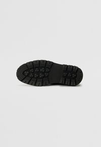 Suela de zapato de goma negra con un patrón de banda de rodadura profundo, que presenta agarraderas circulares y una superficie texturizada para una mayor tracción y durabilidad.