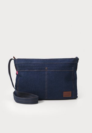Borsa a tracolla in denim blu scuro con dettagli in pelle marrone. Presenta una chiusura con zip e due tasche esterne con cuciture a vista.