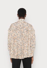Blouse à motif floral avec des accents orange et noir, dotée d'un design plissé, d'un col montant et de larges manches, fabriquée en tissu léger.